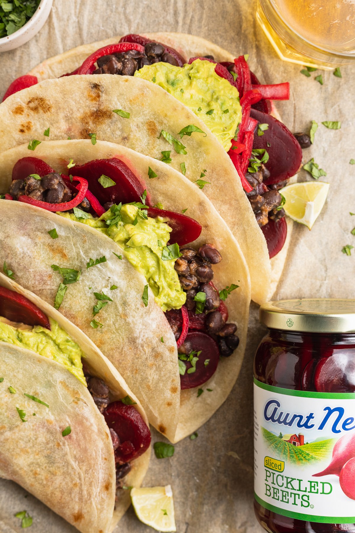Close-up view of 3 pickled beet tacos topped with guacamole next to a jar of pickled beets.