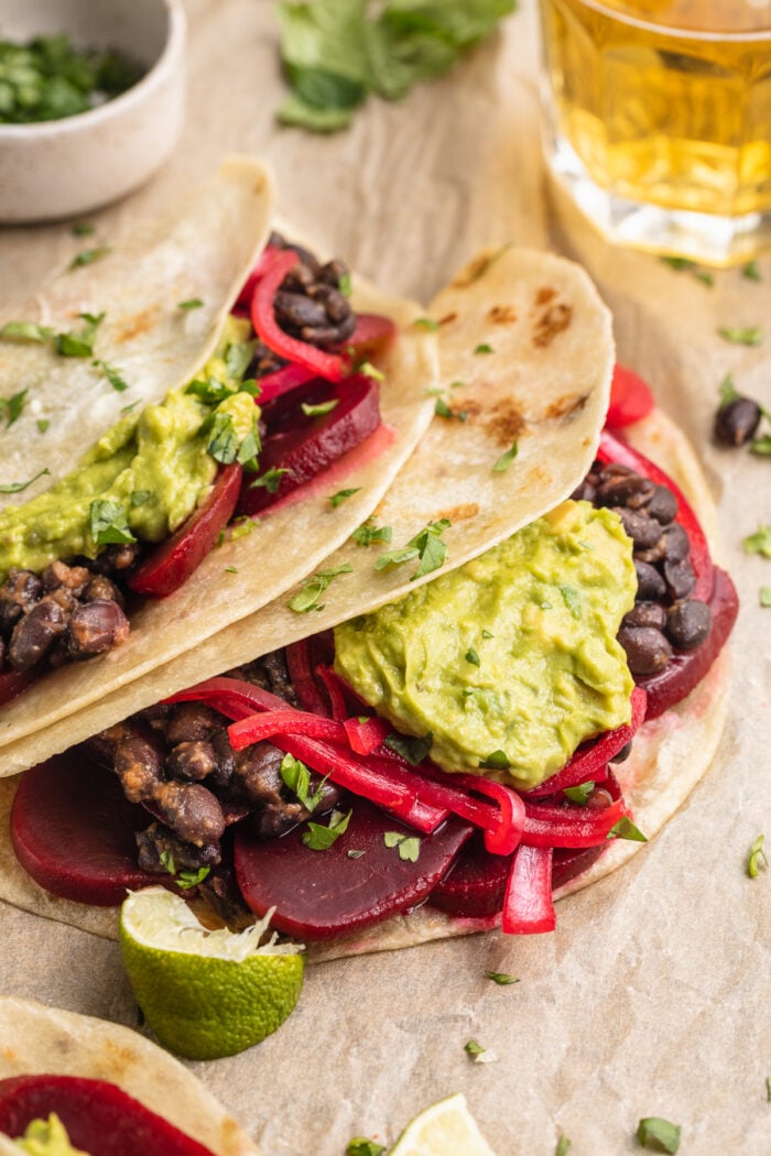 Side angled view of pickled beet tacos with guacamole and a glass of beer.