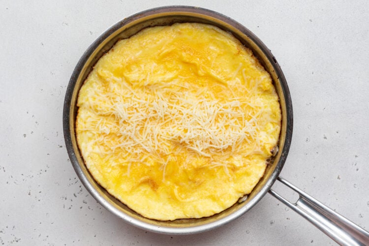 Overhead view of shredded cheese on an omelette in a large silver skillet.