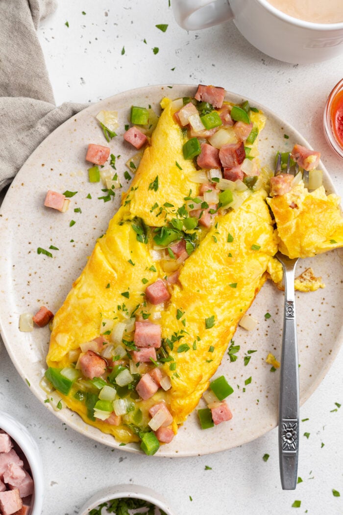 Overhead view of a denver omelette with ham and green onions on a plate surrounded by ingredients.