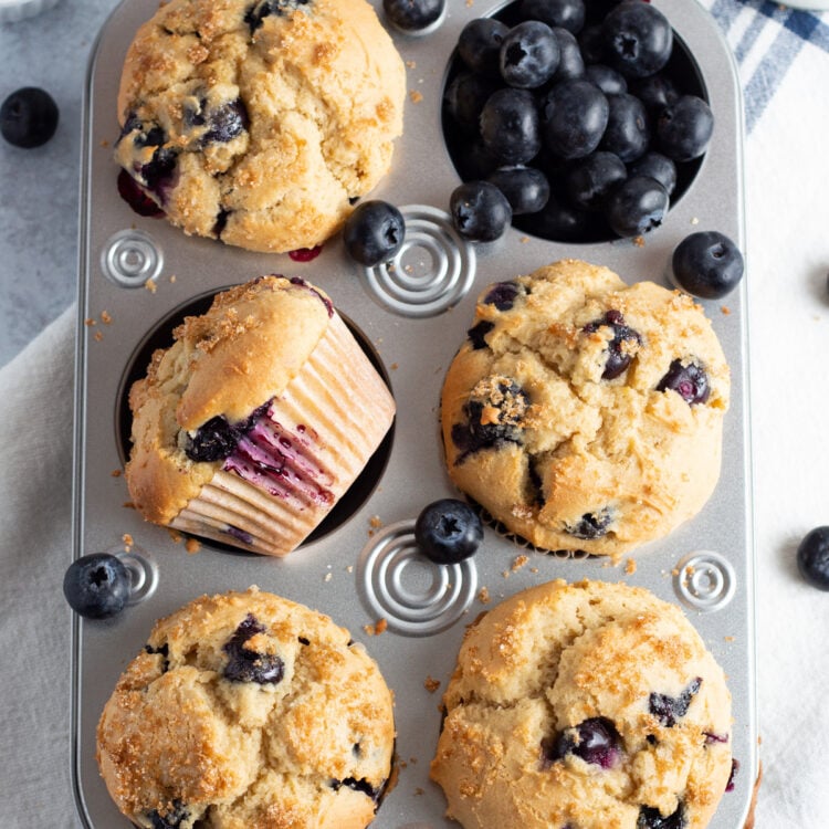Overhead view of a muffin pan with blueberry muffins and a pocket of loose blueberries.