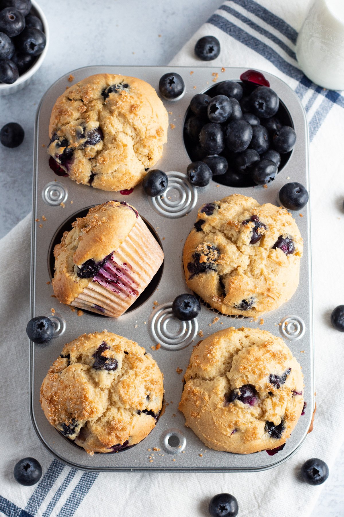 Overhead view of a muffin pan with blueberry muffins and a pocket of loose blueberries.