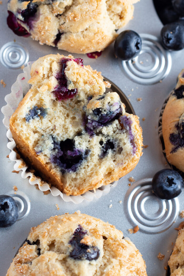 Close-up of a halved gluten free blueberry muffin in a muffin tin with other muffins.