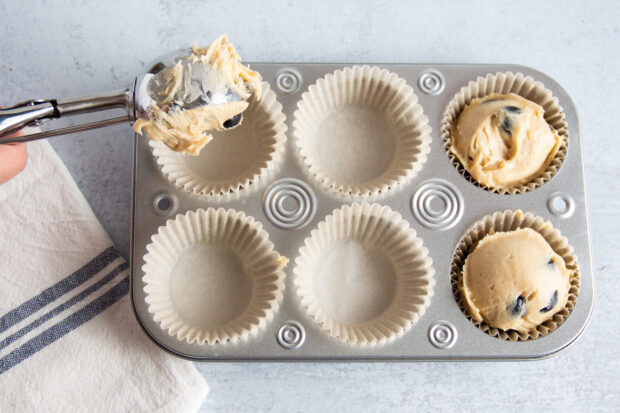 Overhead view of muffin batter added to muffin tin lined with parchment paper baking cups on counter top.