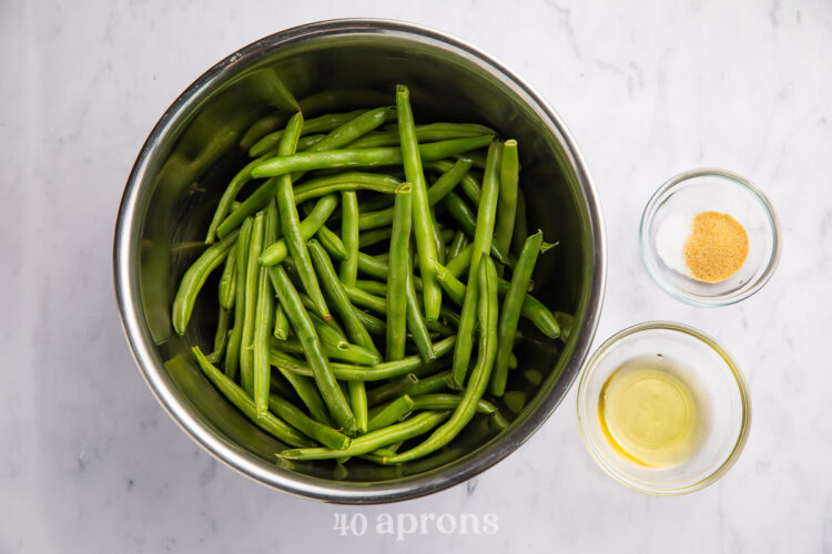 Overhead view of ingredients for air fryer green beans in bowls on white counter.