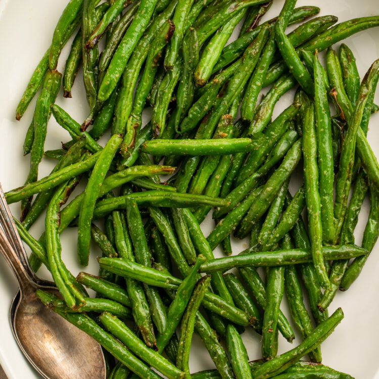 Close-up of air fryer green beans on a white serving platter with lemon wedges and a silver spoon.