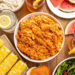 Overhead view of BBQ chicken salad in a bowl surrounded by corn on the cob, watermelon slices, and other barbecue essentials.