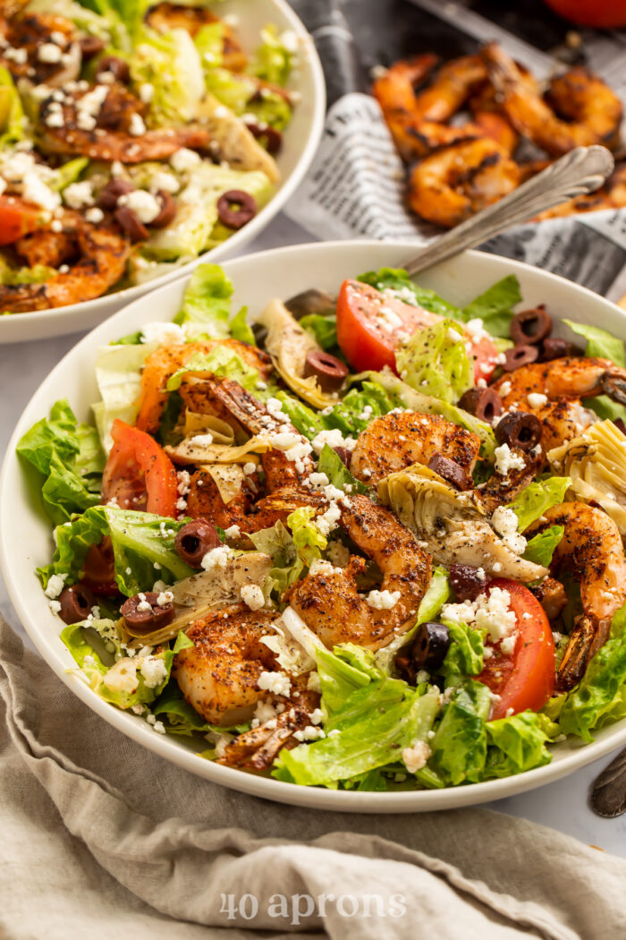 3/4-angle view of a blackened shrimp salad with lettuce, olives, tomatoes, and feta.