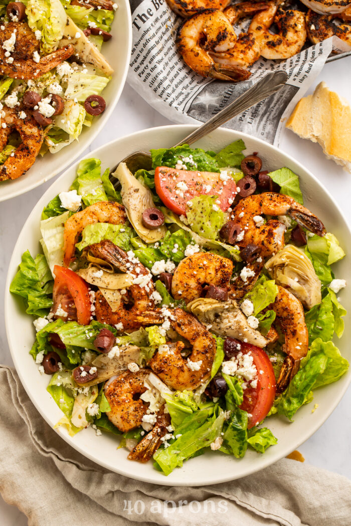 Overhead view of a giant bowl of salad topped with blackened shrimp, kalamata olives, tomato, and feta.