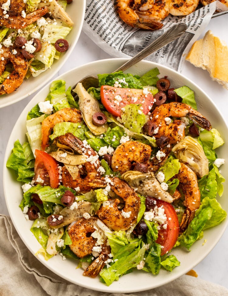 Overhead view of a giant bowl of salad topped with blackened shrimp, kalamata olives, tomato, and feta.