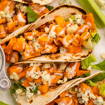 Close-up view of buffalo chicken tacos on a platter with celery and blue cheese dressing.