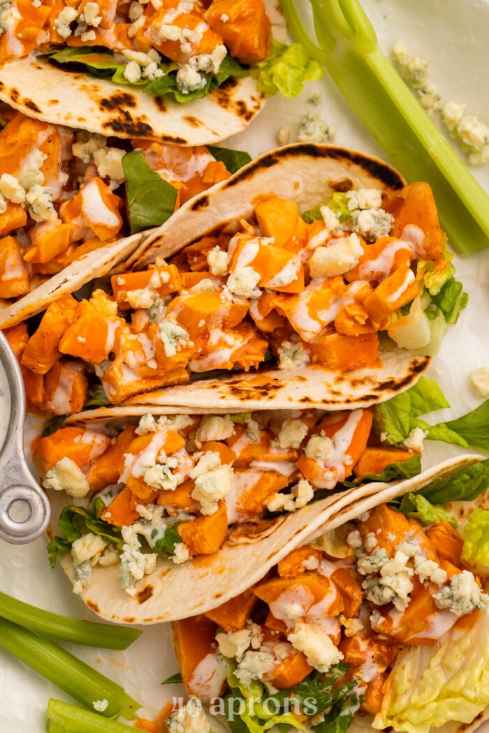 Close-up view of buffalo chicken tacos on a platter with celery and blue cheese dressing.