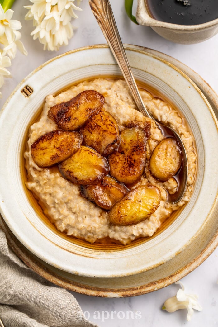 Overhead view of caramelized banana oatmeal in a white bowl on a neutral charger plate.