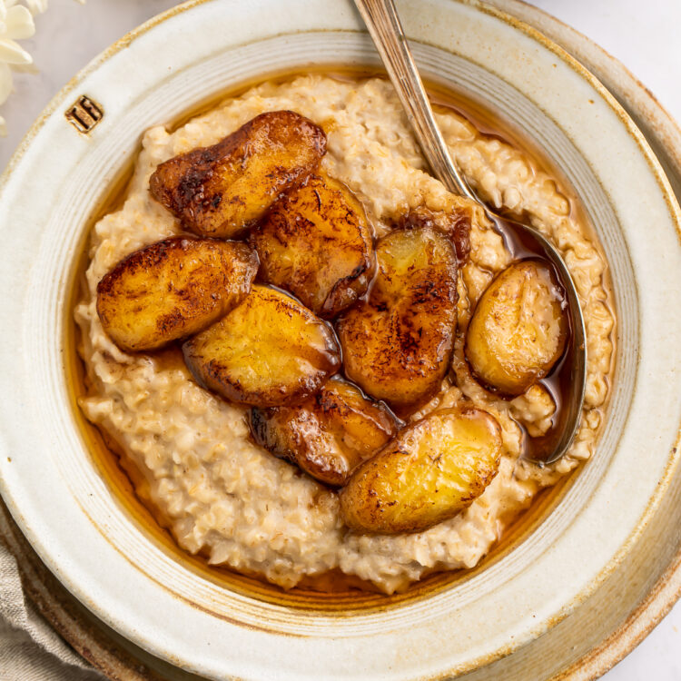 Overhead view of caramelized banana oatmeal in a white bowl on a neutral charger plate.