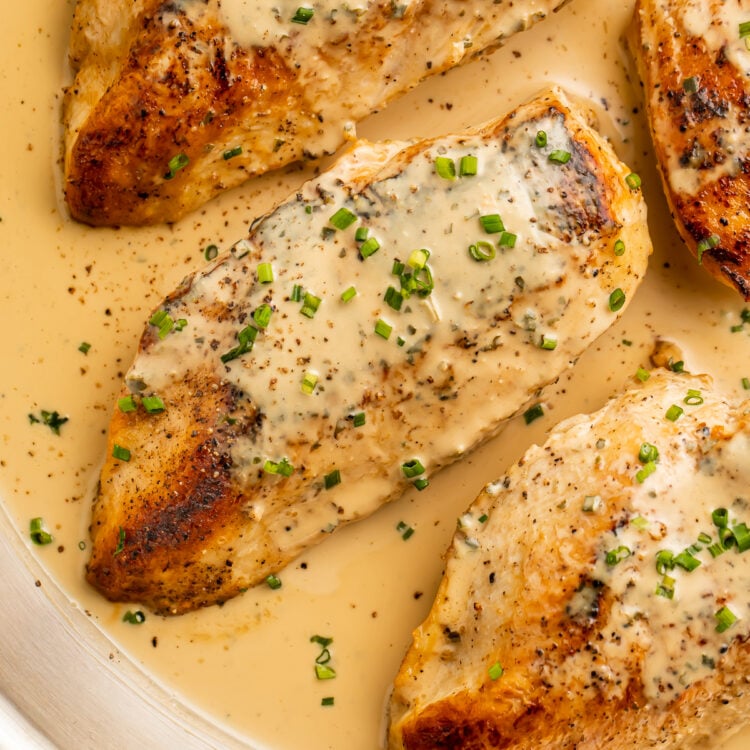 Overhead view of 3 chicken breasts in a skillet with a creamy Boursin sauce and chopped chives.