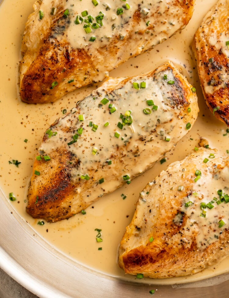 Overhead view of 3 chicken breasts in a skillet with a creamy Boursin sauce and chopped chives.