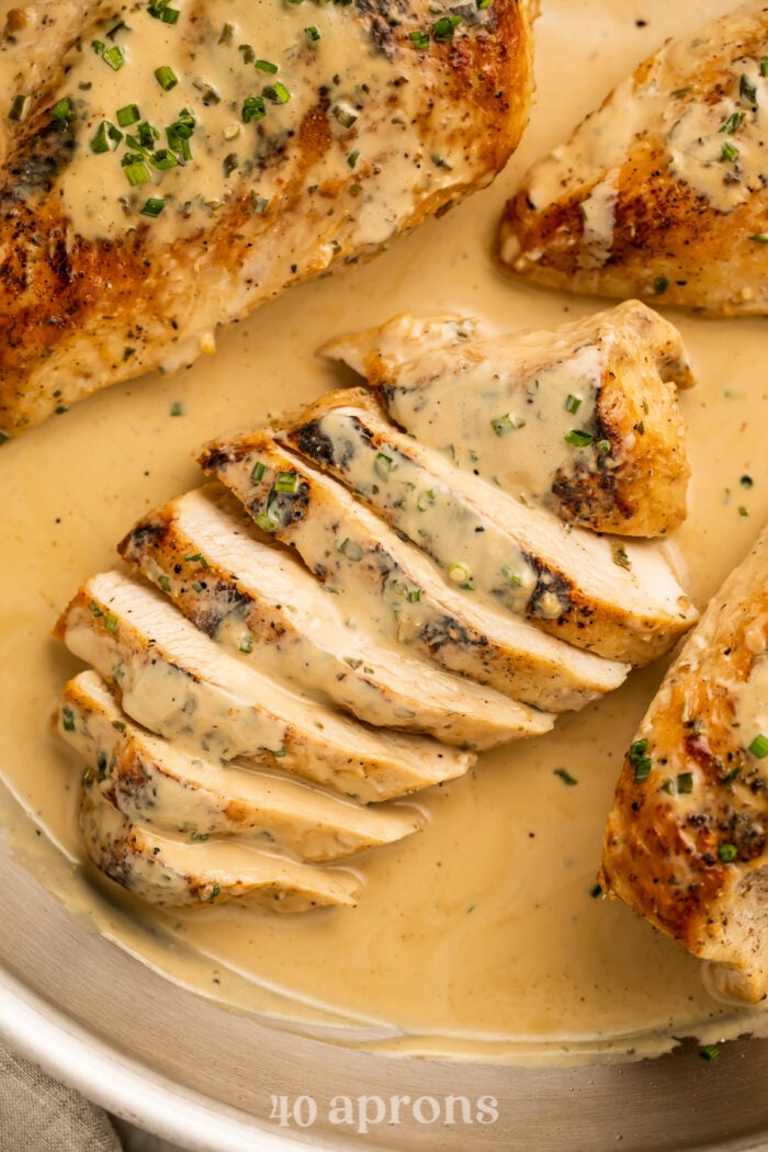 Overhead, close-up view of a sliced chicken breast in a skillet with creamy Boursin sauce and chopped chives.