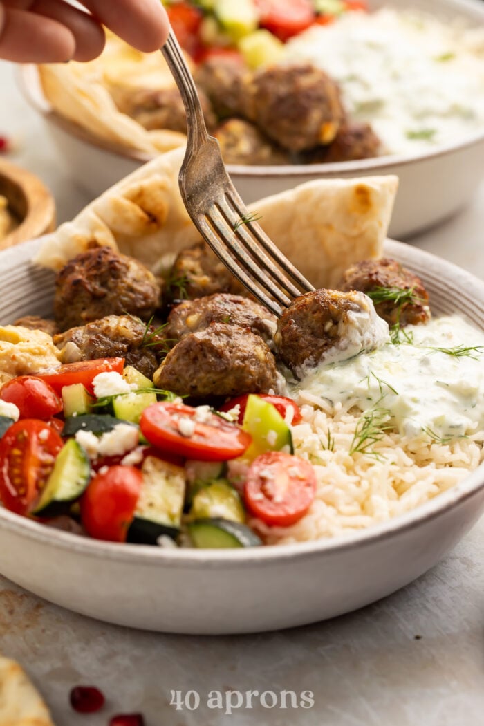 Side view of a gyro bowl with a fork piercing a lamb meatball.