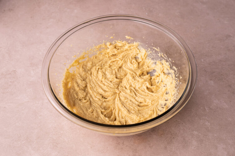 Side-angle view of butter, white sugar, and brown sugar creamed in a large glass mixing bowl on a pink surface.