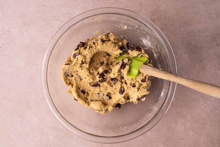 Overhead view of chocolate chip cookie dough in a large glass mixing bowl with a silicone spatula.