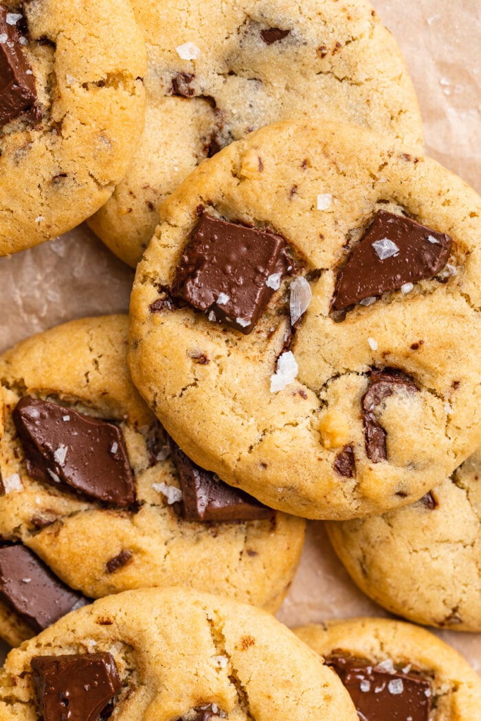 Close-up view of an air fryer chocolate chip cookie with chunks of chocolate and flakes of salt, on a pile of cookies.