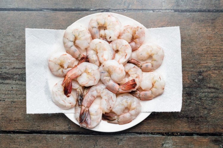 Overhead view of peeled and deveined raw shrimp on a paper towel on a plate.