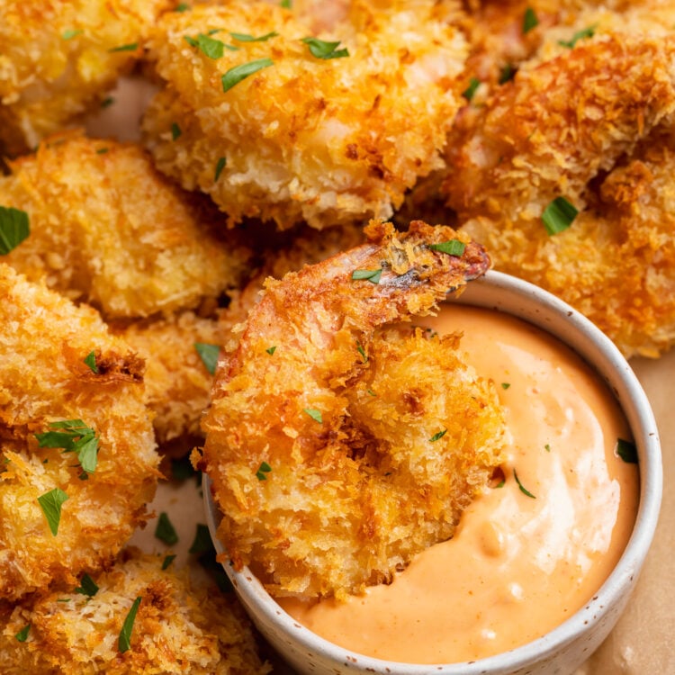 Air fryer shrimp on a neutral plate with a ramekin of sriracha mayo. One shrimp rests in the mayo.