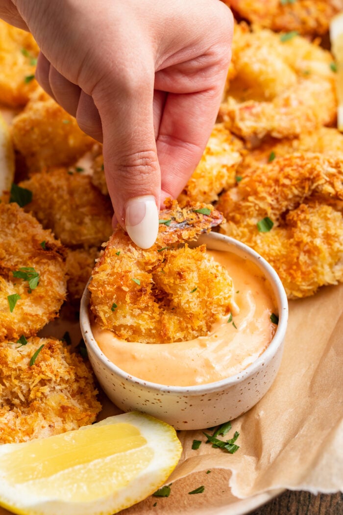 Air fryer fried shrimp being dipped into a small ramekin of sriracha mayo on a platter.