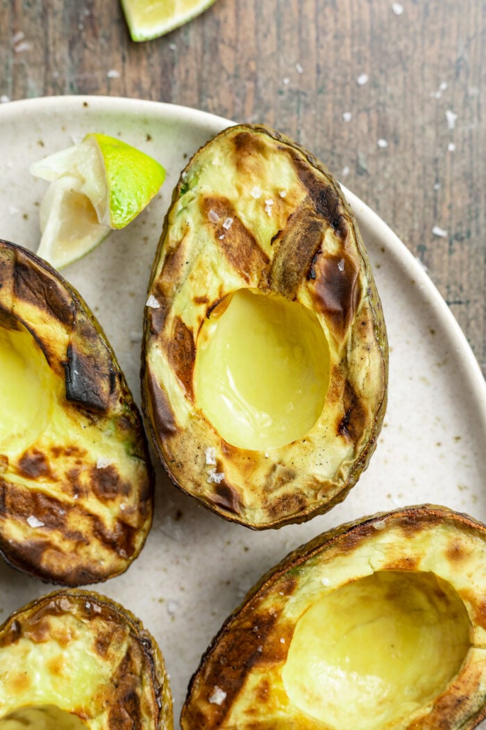 Close-up of a grilled avocado on a plate with lime wedges and other avocados.