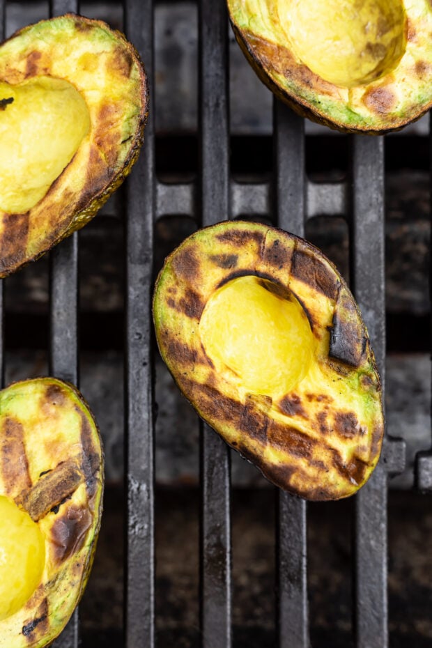 Overhead view of grilled avocado halves on a grill, with black grill marks criss-crossing on avocado meat.