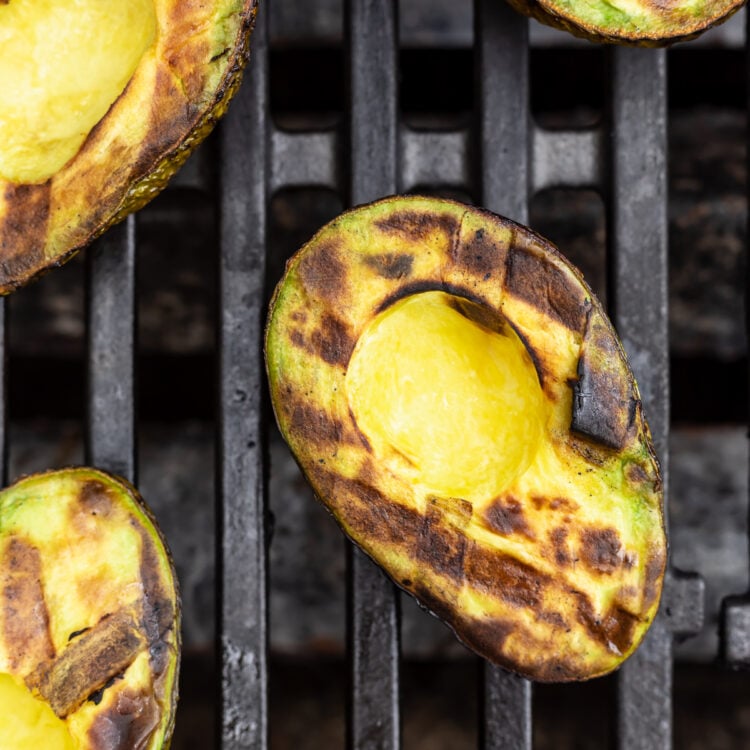Overhead view of grilled avocado halves on a grill, with black grill marks criss-crossing on avocado meat.