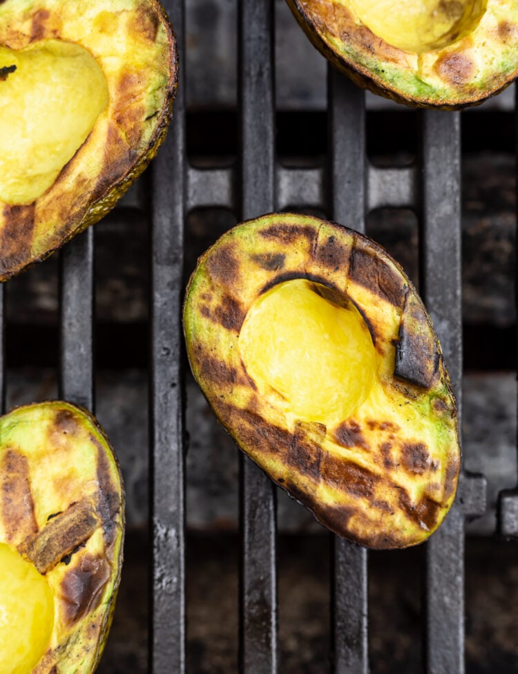 Overhead view of grilled avocado halves on a grill, with black grill marks criss-crossing on avocado meat.