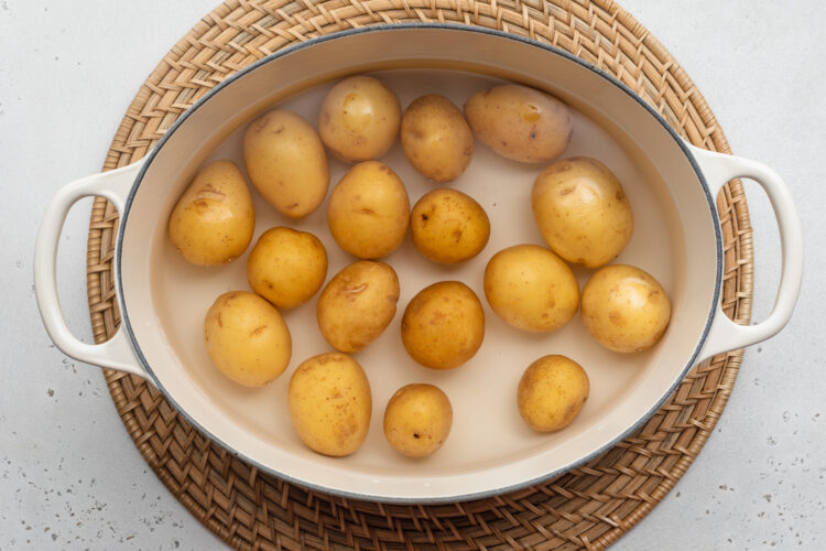 Overhead view of baby potatoes in a large pot with handles on a neutral background.