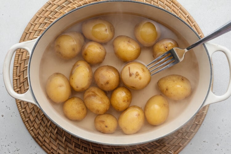 Overhead view of boiling baby potatoes in a large pot on a neutral background.