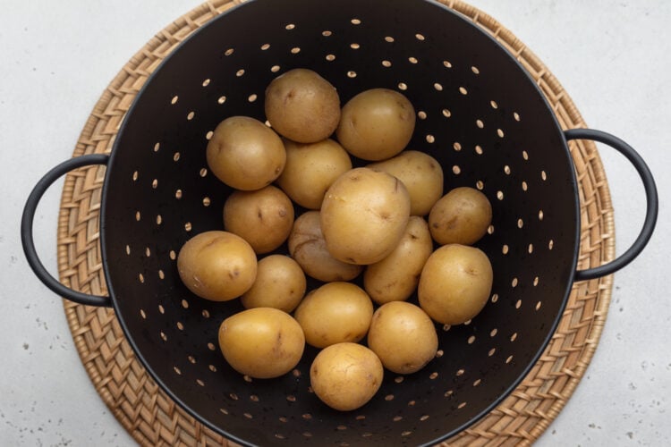 Overhead view of boiled baby potatoes in a large colander on a neutral background.