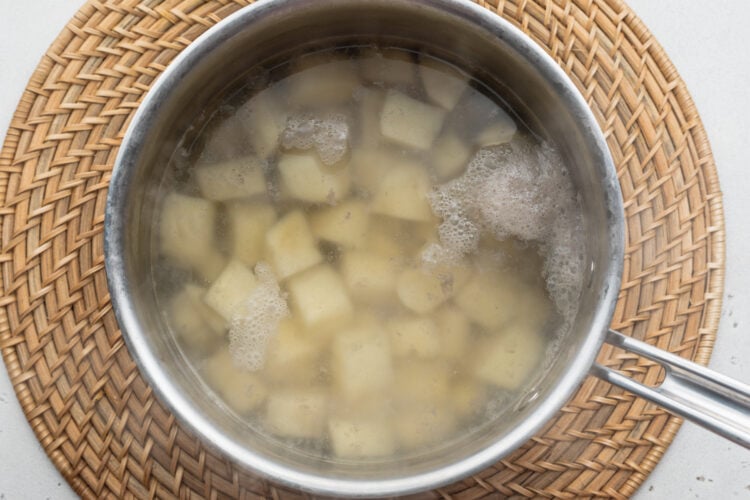 Overhead view of boiled, cubed russet potatoes in a saucepan on a neutral background.