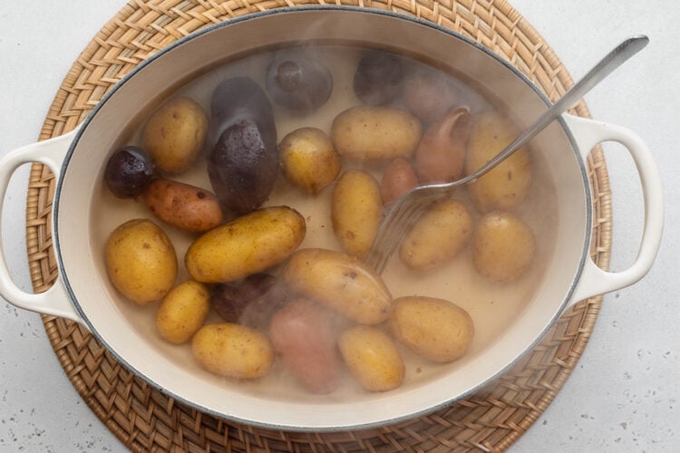 Overhead view of boiling fingerling potatoes in a large pot on a neutral background.