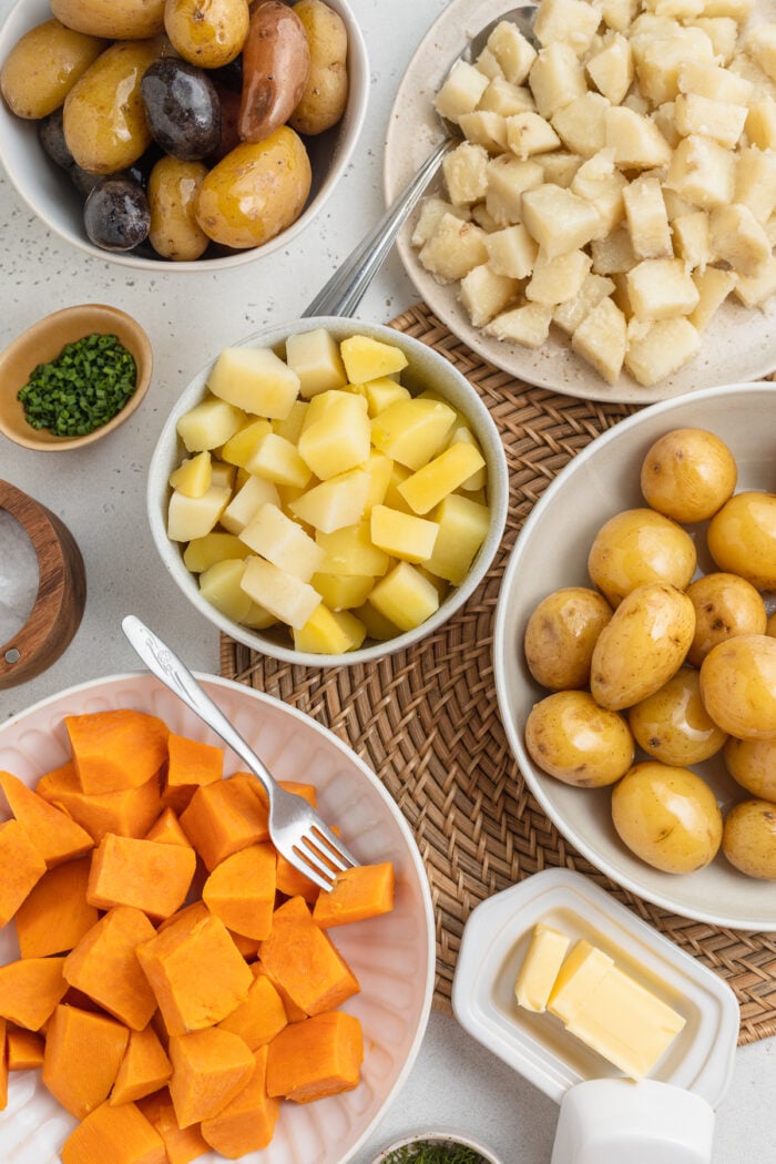 Overhead view of several varieties of boiled potatoes in bowls arranged together on a table.