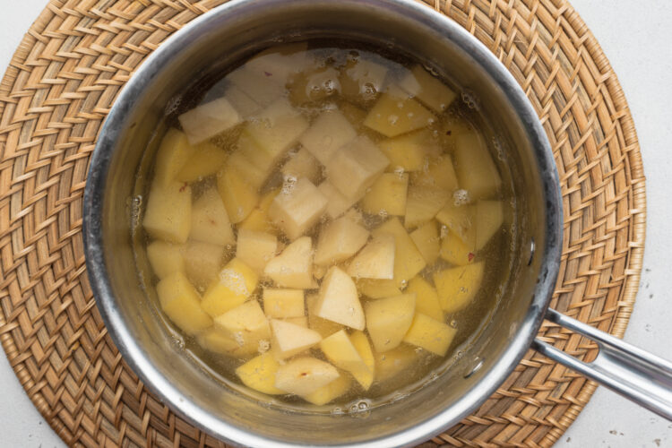 Overhead view of cubed potatoes in a saucepan on a neutral background.