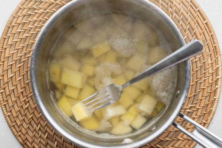 Overhead view of boiled, cubed potatoes in a saucepan on a neutral background.
