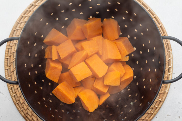 Overhead view of boiled sweet potato cubes in a large black colander/