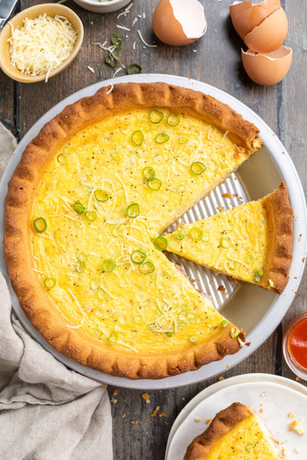 Overhead view of keto quiche in a pie crust plate, with one slice of quiche missing and another separated from the rest.