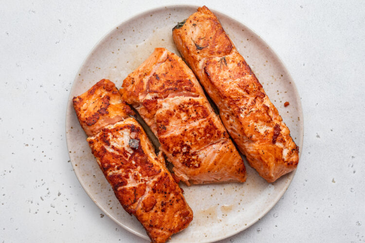 Overhead view of seasoned, pan-seared, sous vide salmon fillets on a white plate.
