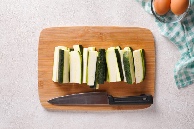 Overhead view of zucchini sticks on a wooden cutting board.