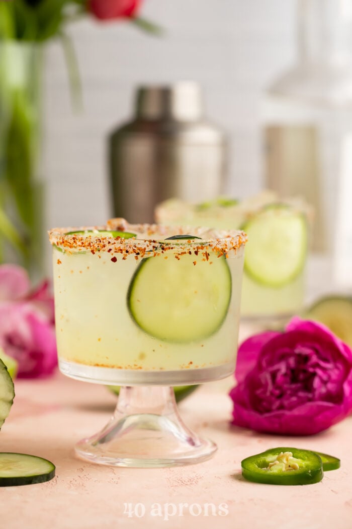 Cucumber jalapeno margarita in a short glass with cucumber slices and a deep fuschia flower.