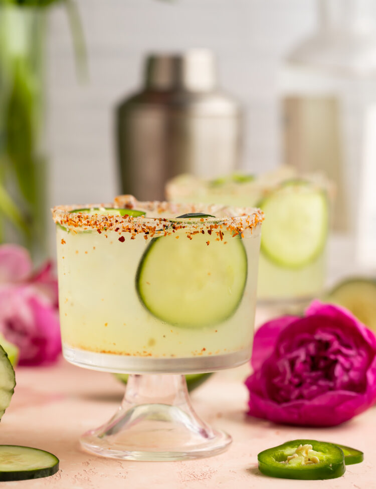 Cucumber jalapeno margarita in a short glass with cucumber slices and a deep fuschia flower.