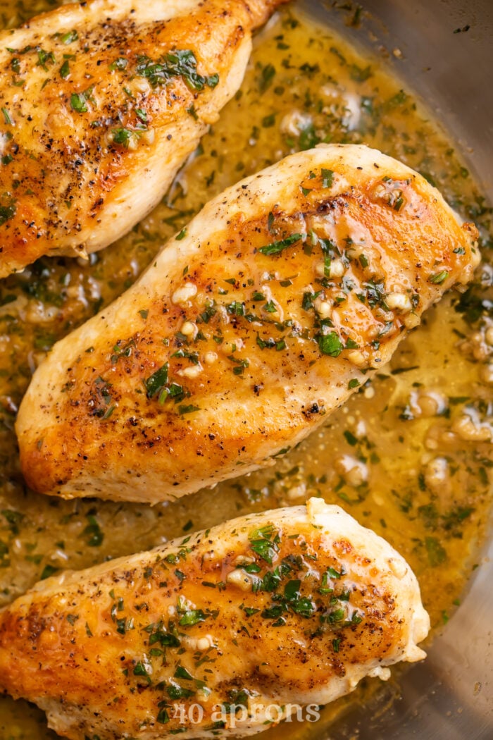 Overhead view of a whole garlic butter chicken breast in garlic butter sauce in a silver skillet.