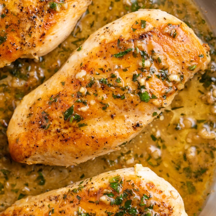 Overhead view of a whole garlic butter chicken breast in garlic butter sauce in a silver skillet.