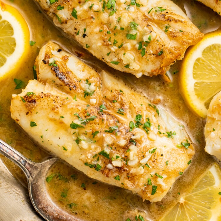Overhead view of garlic butter cod filets in a silver skillet with garlic butter sauce and lemon coins.