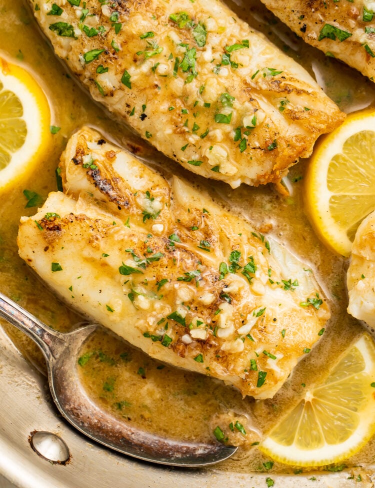 Overhead view of garlic butter cod filets in a silver skillet with garlic butter sauce and lemon coins.